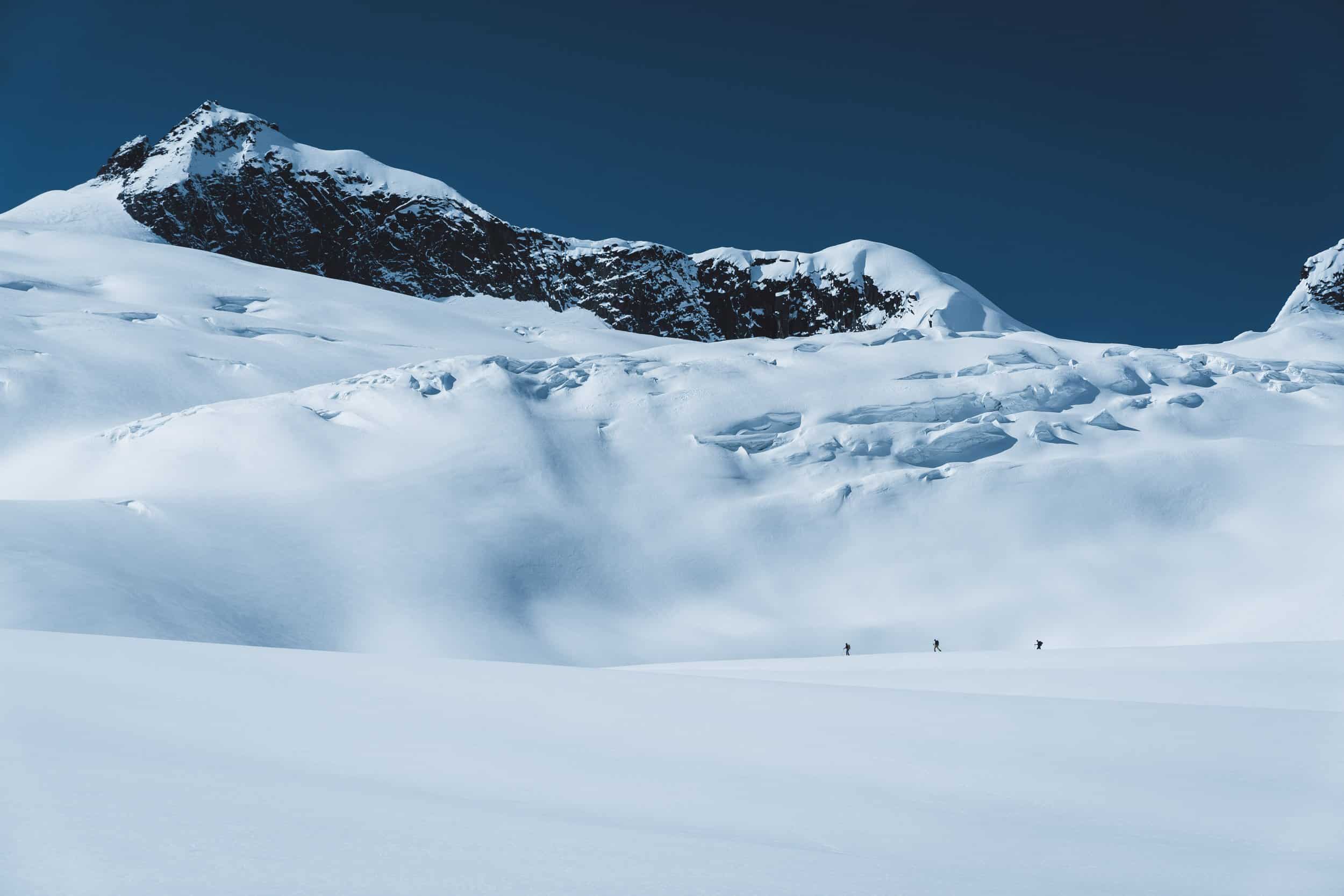 Three skiiers in the far distance of a snowy mountain scene.