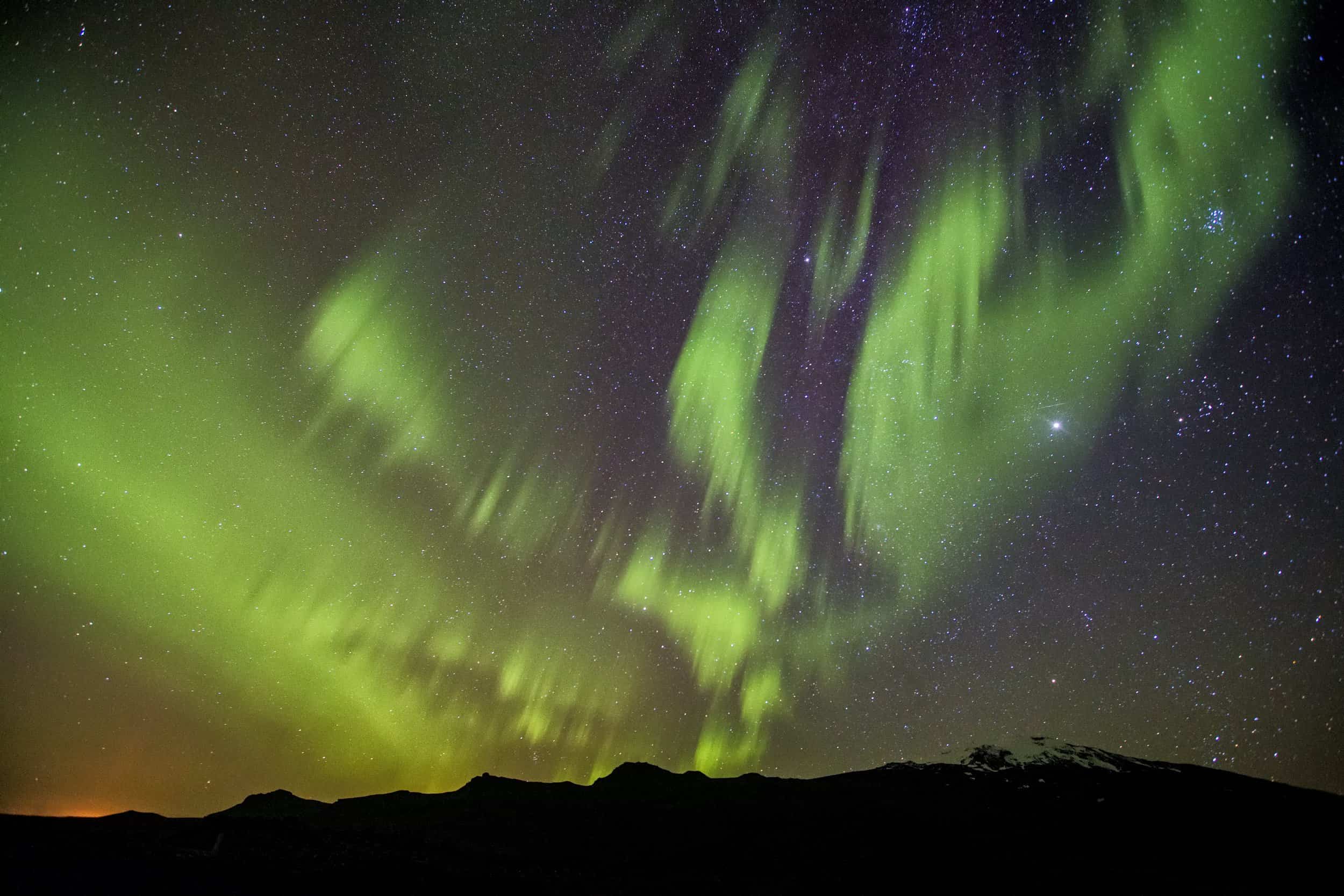 Photo of the northern lights with mountains in silhouette.