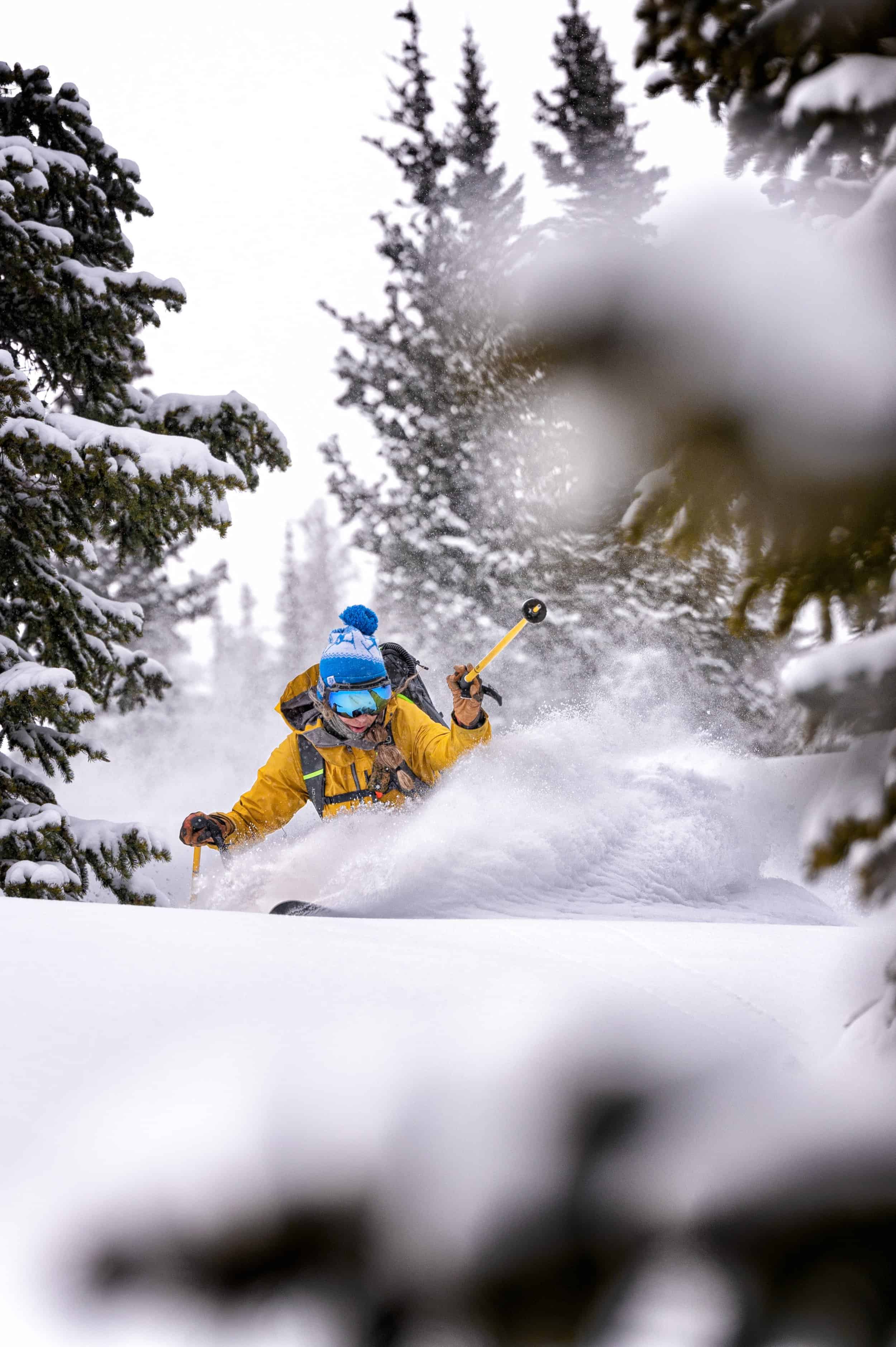 Skier carves turns in powder wearing yellow parka and blue beanie