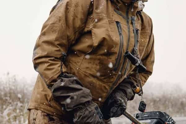 A rugged hunter dressed in outdoor gear, preparing for a hunting or outdoor adventure in a snowy landscape.