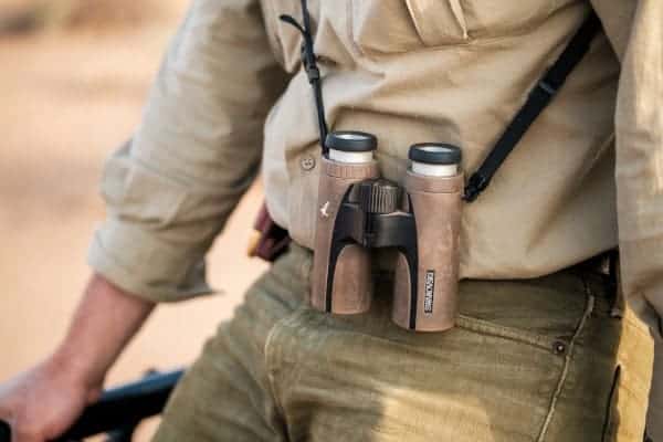 Binoculars in a beige holster, outdoor hunting gear, modern huntsman equipment, wilderness exploration, nature observation gear.